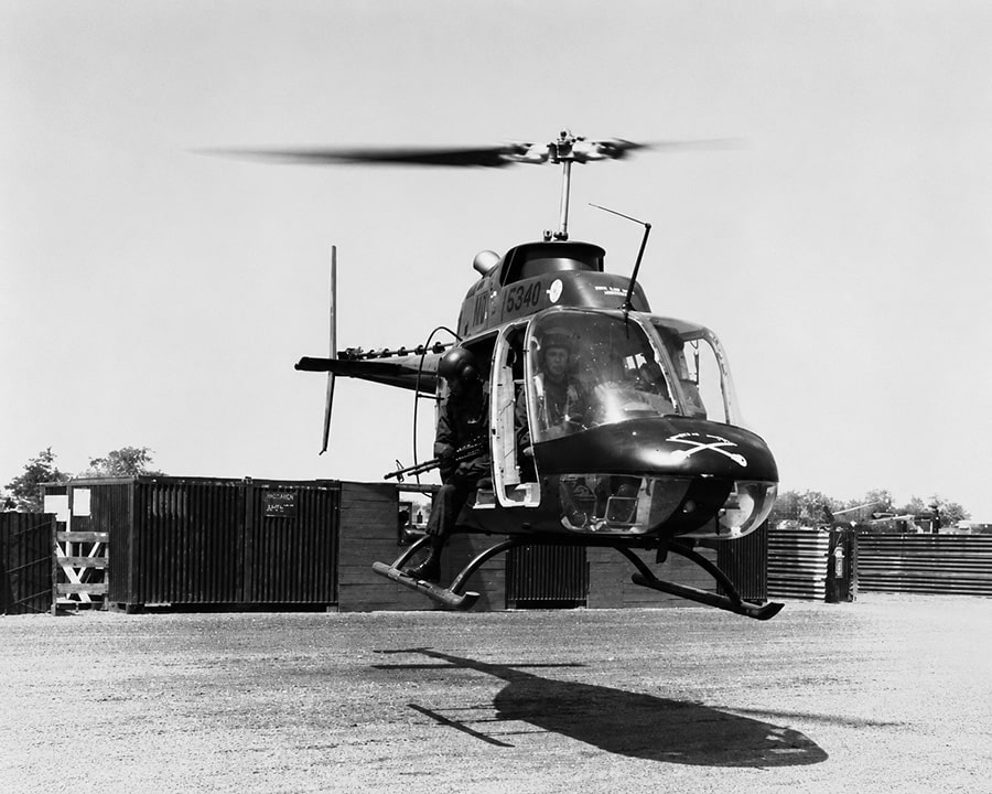 Black-and-white image of a Bell OH-58 Kiowa light reconnaissance helicopter lifting off from a military base during the Vietnam War era.