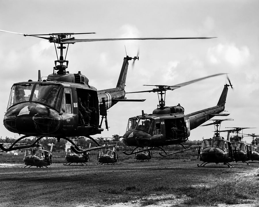 Black-and-white image of multiple Bell UH-1 Huey helicopters lifting off from a Vietnam War airfield before a combat mission.