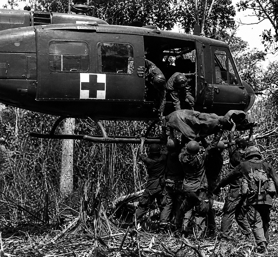 Black-and-white image of a Bell UH-1 Huey Dustoff medevac helicopter loading a wounded soldier during Vietnam War operations.