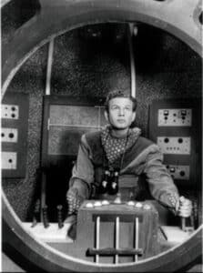 Frankie Thomas as Tom Corbett operating controls aboard the Polaris with space binoculars around his neck.